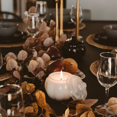 Decorative table setting with candles, glasses, and leaves on a dark surface.