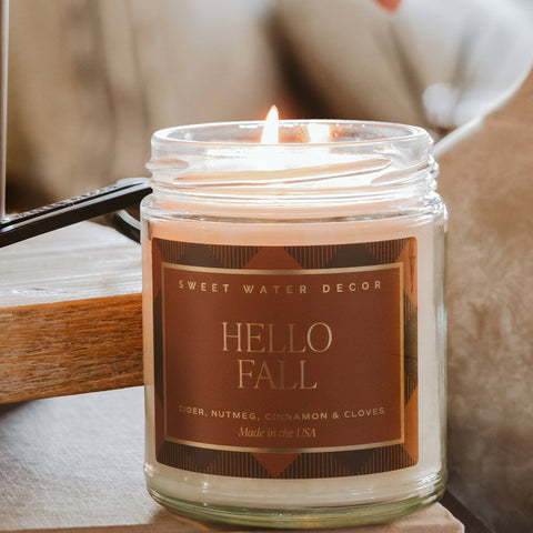 Candle in a jar with 'Hello Fall' label on a wooden surface