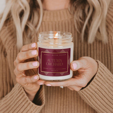 Person holding a 'Autumn Orchard' candle with a warm background
