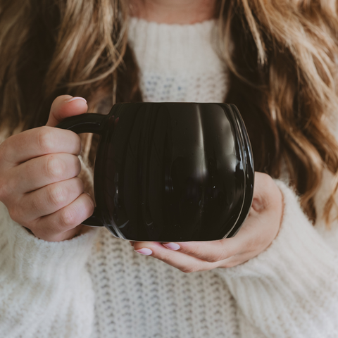 Person holding a black pumpkin shaped mug with a blurred background