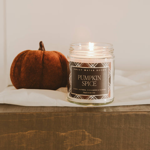 Pumpkin spice candle with a small pumpkin on a wooden surface