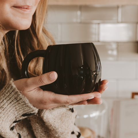 Person holding a black mug in a kitchen setting