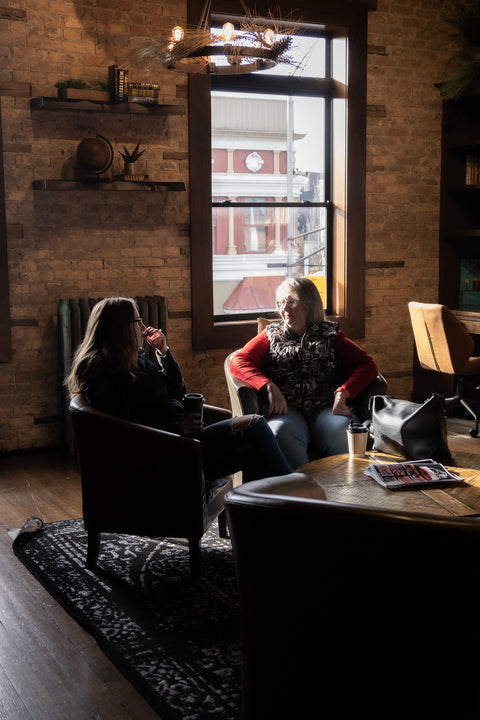 Two people sitting in a cozy room with a large window, talking.