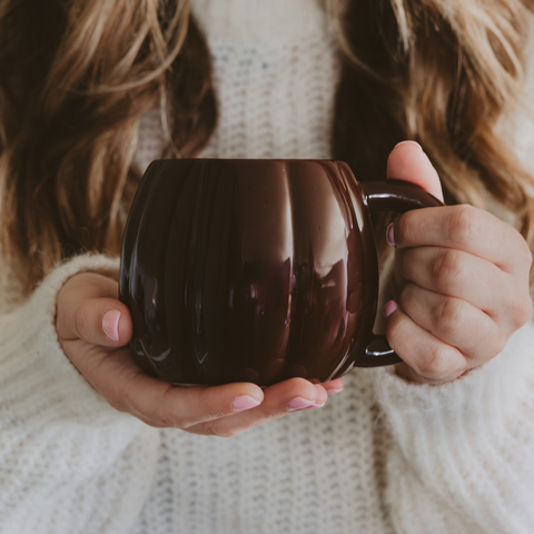 Person holding a dark brown mug with a blurred background