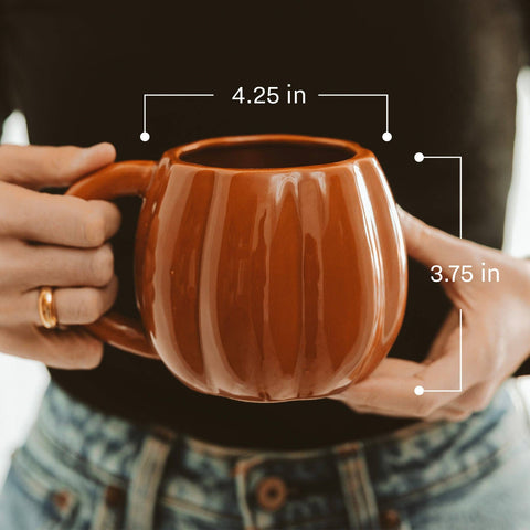 Brown ceramic mug held by hands with measurements indicated.