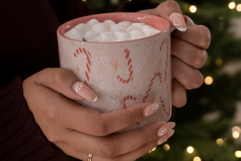 Woman's hands holding pink candy cain mug containing hot chocolate and marshmallows