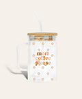 Clear glass mug with a handle, bamboo lid, and clear straw, featuring the text 'more coffee please' in orange and small floral motifs, on a light beige background.
