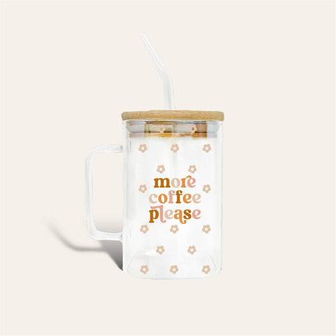 Clear glass mug with a handle, bamboo lid, and clear straw, featuring the text 'more coffee please' in orange and small floral motifs, on a light beige background.