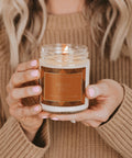 Person holding a 'Hello Fall' candle with a warm, autumnal design.