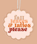 A scalloped oval hanging air freshener with the phrase 'fall leaves & lattes please' in decorative autumn-colored lettering, suspended by a thin white string against a warm beige background.