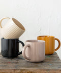 Four ceramic mugs in different colors stacked on a wooden surface with a white background