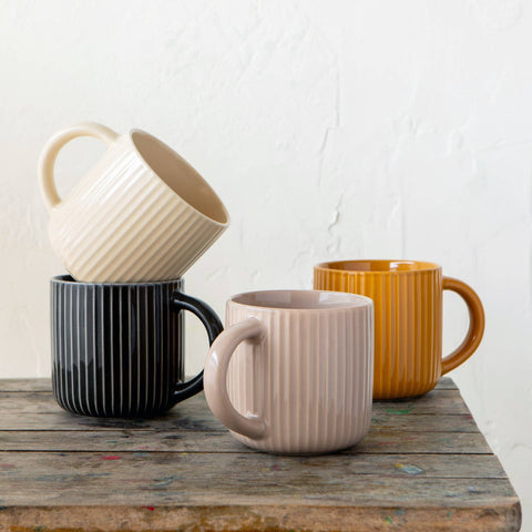 Four ceramic mugs in different colors stacked on a wooden surface with a white background