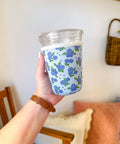 Hand holding a cup with a floral pattern sleeve against a neutral background