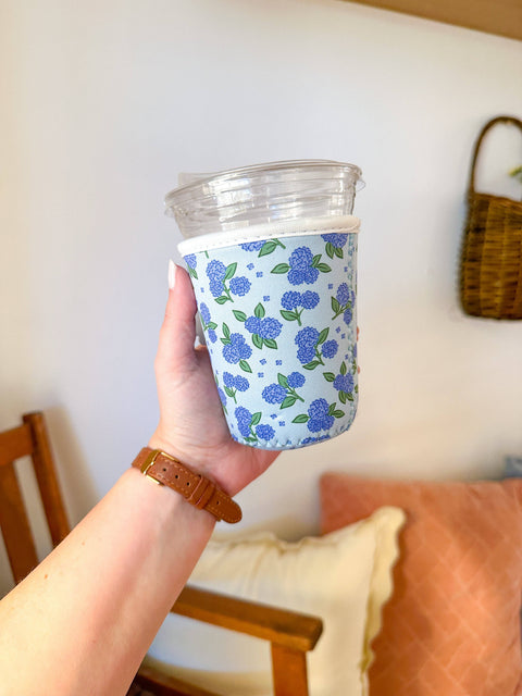 Hand holding a cup with a floral pattern sleeve against a neutral background