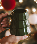Green mug held by a hand with festive lights in the background