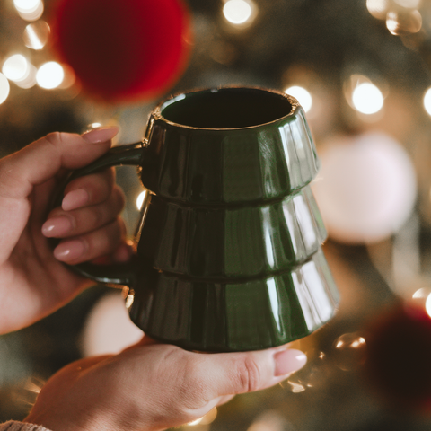 Green mug held by a hand with festive lights in the background