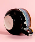 Black ceramic mug with a colorful handle on a pink background