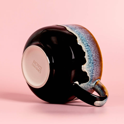 Black ceramic mug with a colorful handle on a pink background