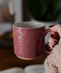 Person holding a pink mug with floral patterns in a cozy indoor setting