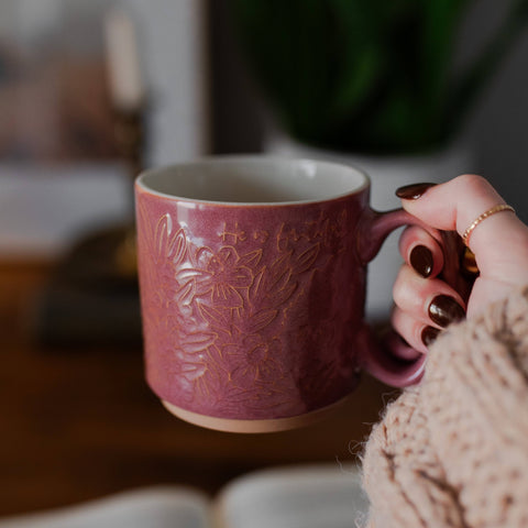 Person holding a pink mug with floral patterns in a cozy indoor setting