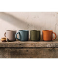 Four ceramic mugs in different colors on a wooden surface with a neutral background