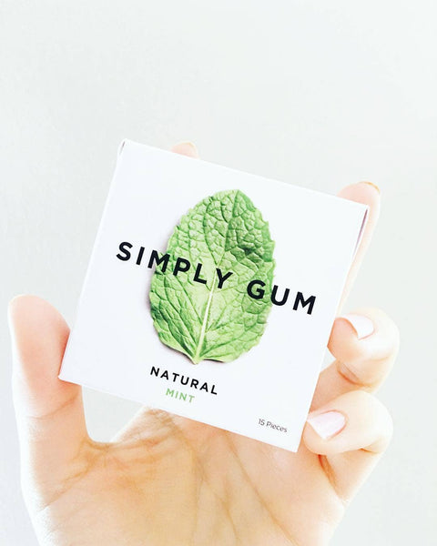 Hand holding a package of Simply Gum with a mint leaf on a white background