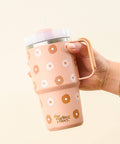 Hand holding a tan mug with floral patterns and 'the darling effect' branding on a light background