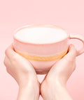 Pink mug with a white interior held by hands against a pink background