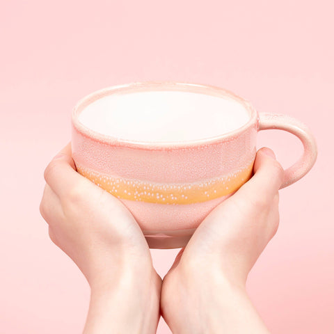 Pink mug with a white interior held by hands against a pink background