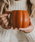 Woman holding a pumpkin mug in a cozy setting