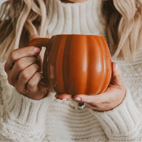 Woman holding a pumpkin mug in a cozy setting