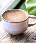 Cup of coffee with a decorative handle on a wooden surface with green leaves in the background