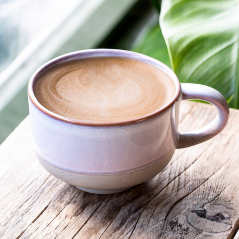 Cup of coffee with a decorative handle on a wooden surface with green leaves in the background