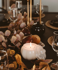 Decorative table setting with candles, glasses, and leaves on a dark surface.