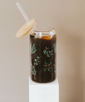 Glass tumbler with floral design filled with a dark liquid, on a beige background