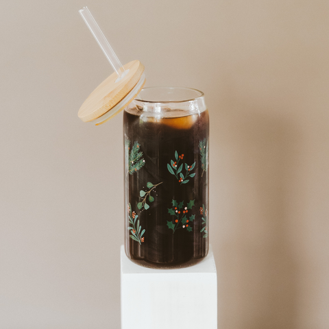 Glass tumbler with floral design filled with a dark liquid, on a beige background