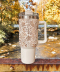 Tumbler with pumpkin pattern in an outdoor setting with trees and water.