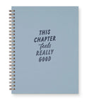 A light blue spiral notebook with a silver wire binding and the text 'THIS CHAPTER feels REALLY GOOD' printed on the front cover, shown against a plain white background.