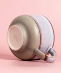 Speckled ceramic cup with multi color exterior on a pink background, featuring the Nova Ceramics logo.