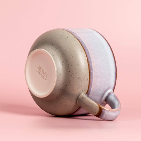 Speckled ceramic cup with multi color exterior on a pink background, featuring the Nova Ceramics logo.