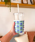 Hand holding a clear cup with a floral patterned sleeve against a neutral background
