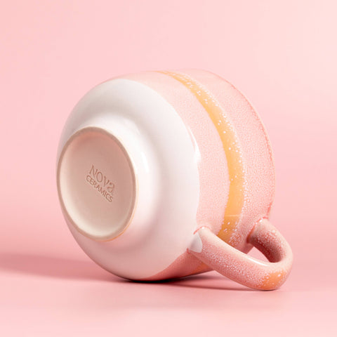 Pink ceramic mug with a textured handle on a pink background, featuring the Nova Ceramics logo.