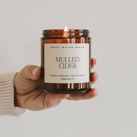 Hand holding a 'Mulled Cider' candle with a label on a neutral background