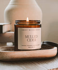 Candle labeled 'Mulled Cider' by Sweet Water Decor on a wooden tray with books and glasses in the background.