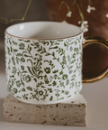 White mug with green floral pattern on a stone surface
