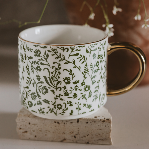 White mug with green floral pattern on a stone surface