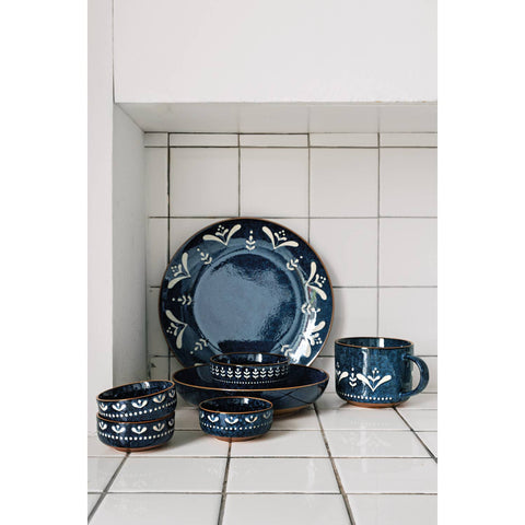 Set of blue ceramic dinnerware with white patterns on a tiled kitchen floor.