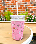 Pink tumbler with a floral pattern on a wooden table outdoors.