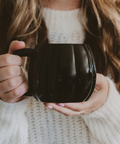 Person holding a black pumpkin shaped mug with a blurred background