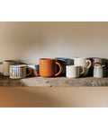 Collection of ceramic mugs on a wooden shelf with a neutral background